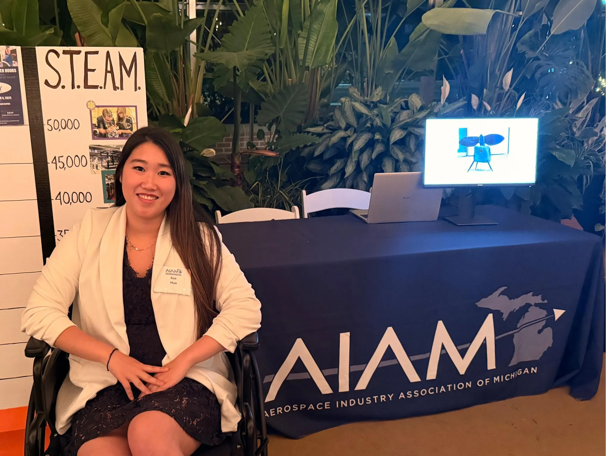 Seated beside the AIAM table at a S.T.E.A.M. event, with a model aircraft on screen behind