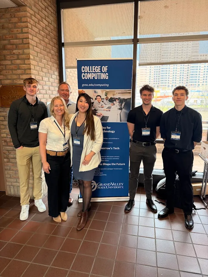 Six people standing in front of a Grand Valley State University College of Computing banner