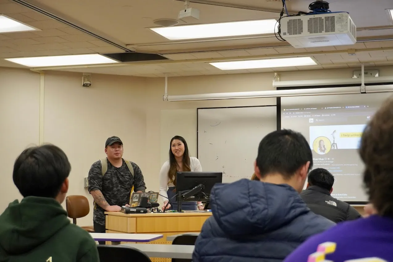 Standing beside a co-presenter in a campus classroom, a BobaTalks profile slide projected behind