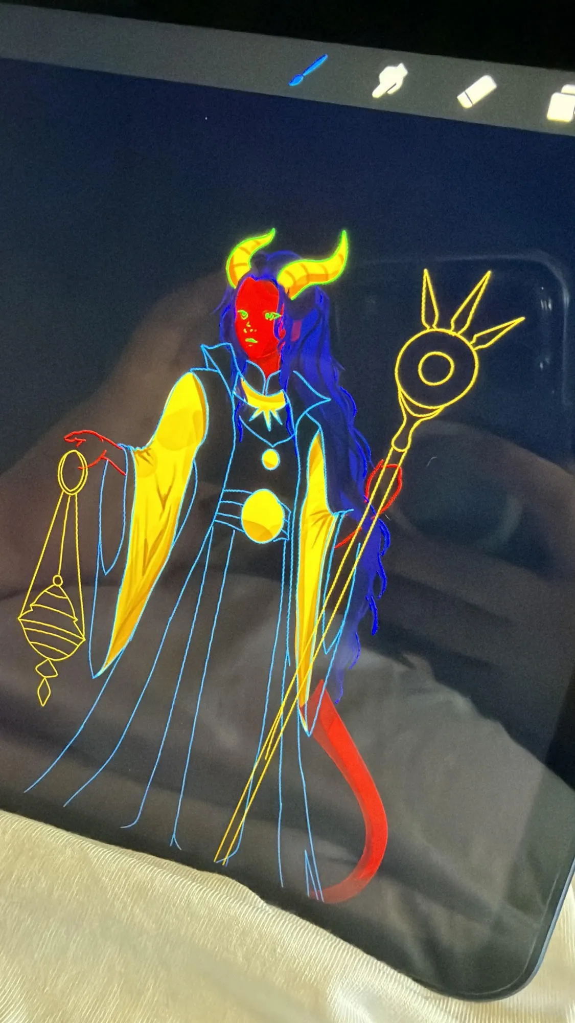 An iPad resting on a lap, its screen showing a character drawn as inverted neon line work: glowing blue, yellow, and red outlines of a horned figure with long hair, holding a staff and a hanging lantern against a dark canvas.