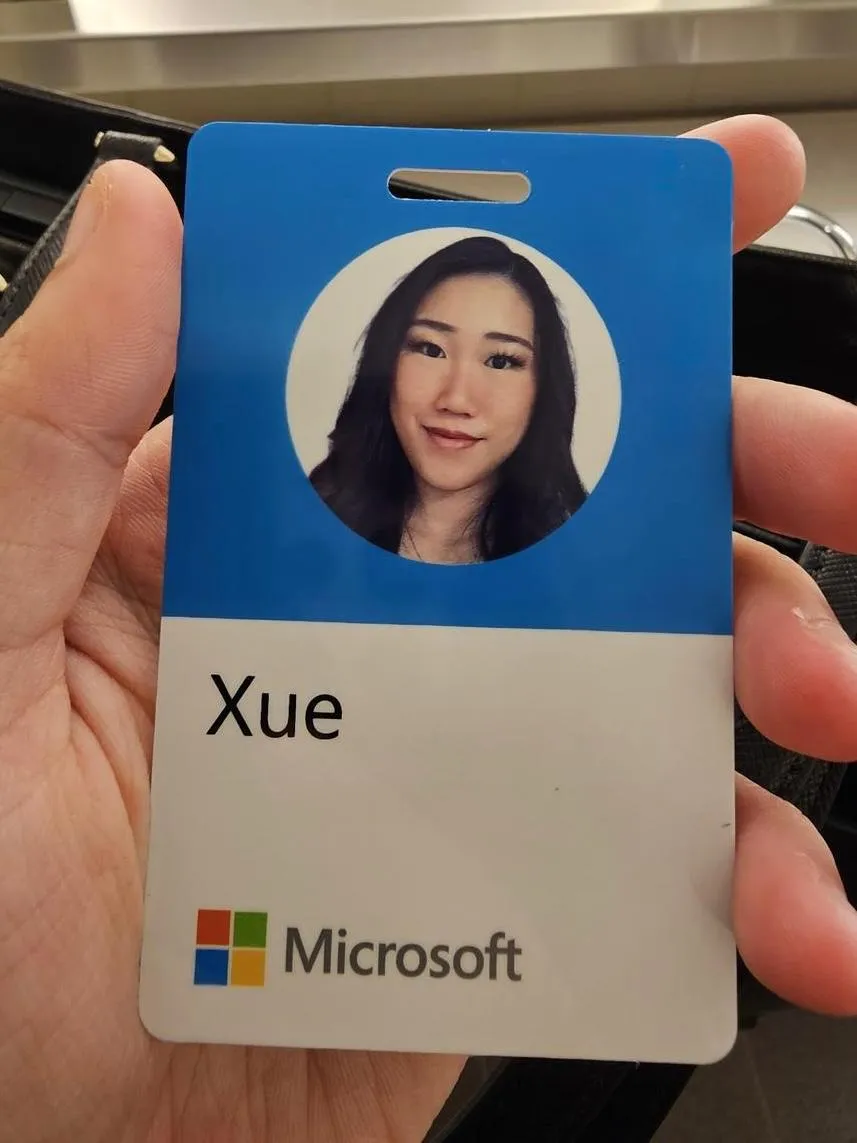 A hand holds a Microsoft employee badge showing Xue's name and headshot, with the four-square Microsoft logo on a white card and blue header band.