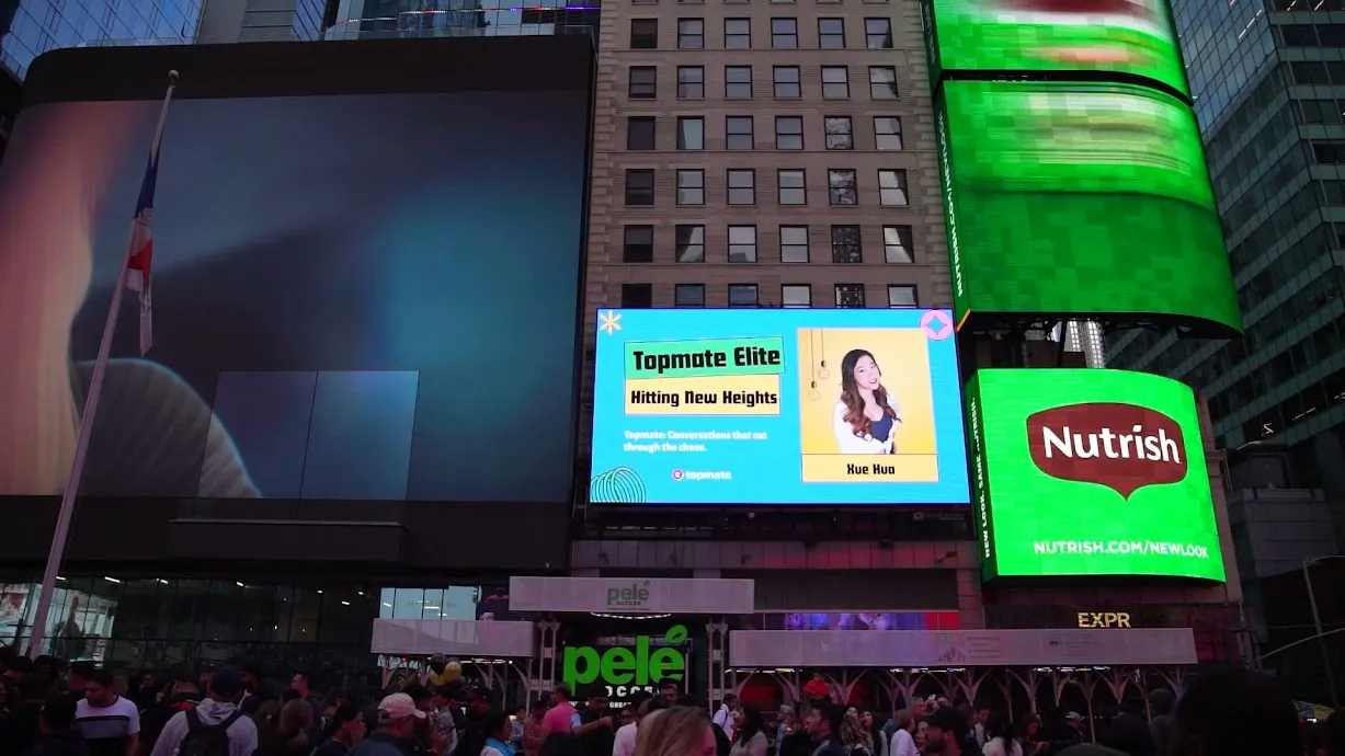 A Topmate Elite "Hitting New Heights" billboard featuring Xue Hua, lit up in Times Square