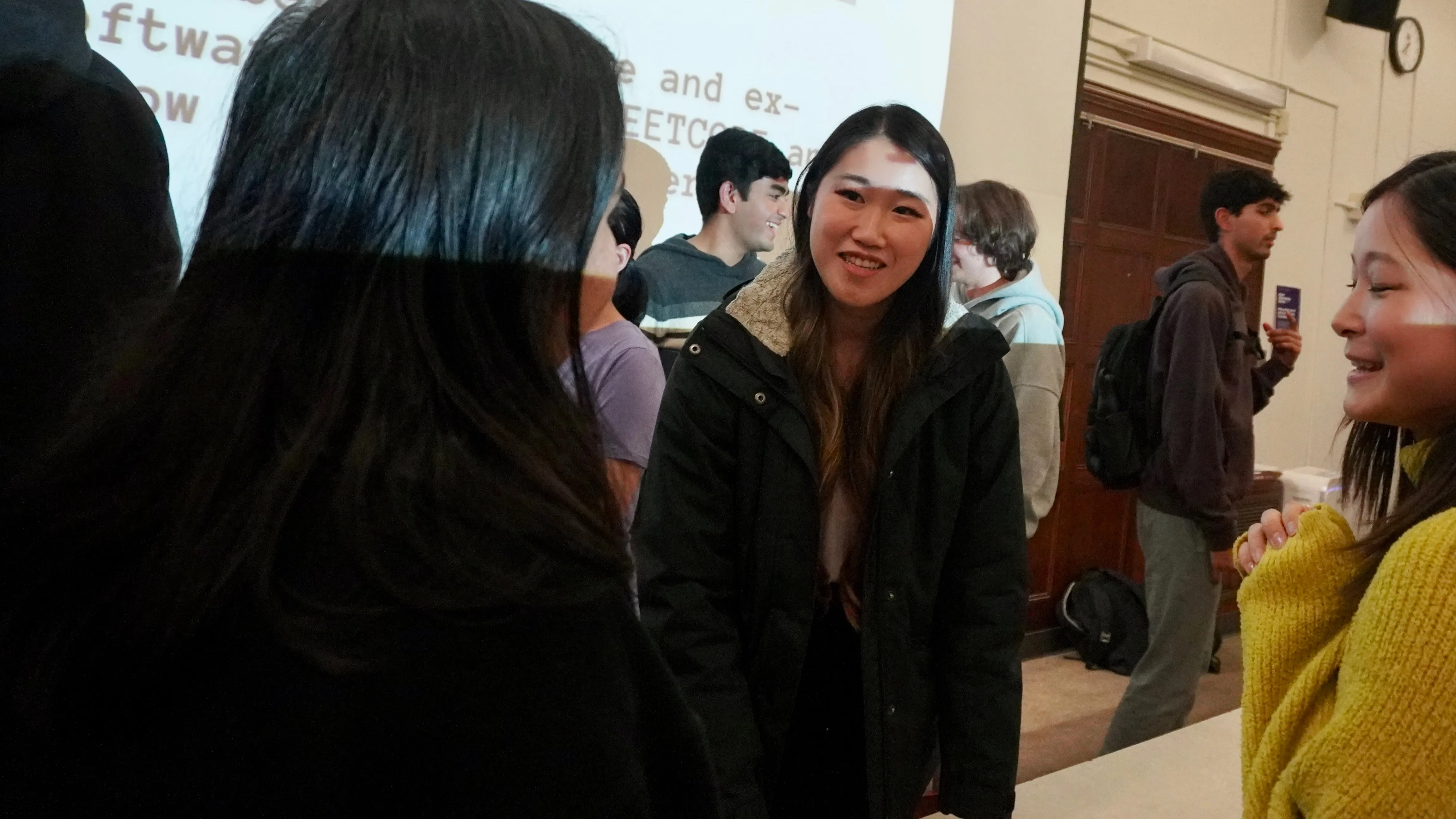 In conversation with students after a talk, partial slide visible behind
